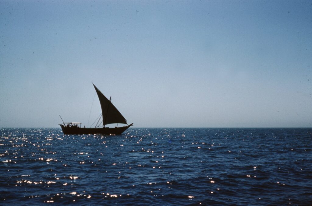 black sail boat on sea under gray sky